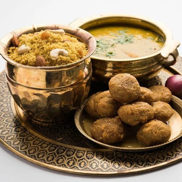 Traditional Indian meal with dal baati churma served in brass bowls on an ornate tray.
