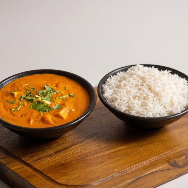 Two black bowls on a wooden board, one with orange curry and the other with white rice.