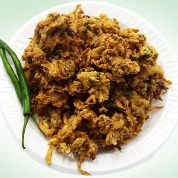 Crispy golden-brown pakoras, garnished with two vibrant green chilies on a white plate.