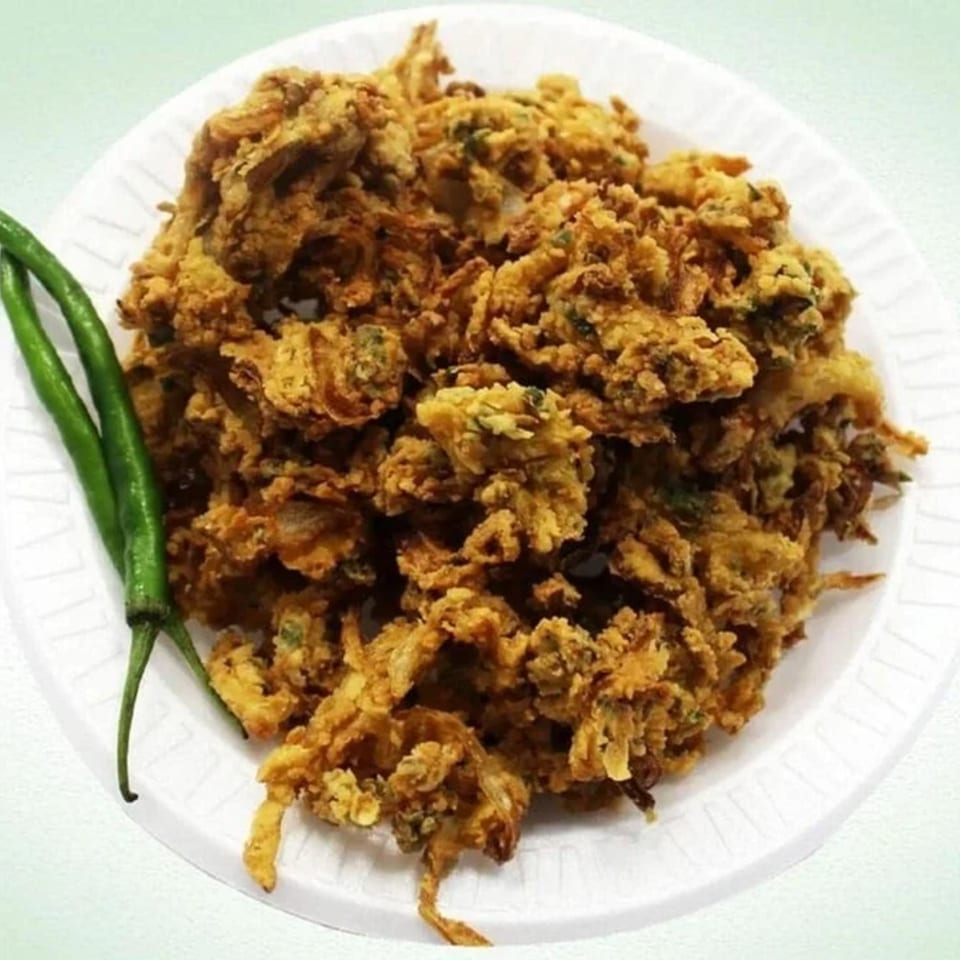 Crispy golden-brown pakoras, garnished with two vibrant green chilies on a white plate.