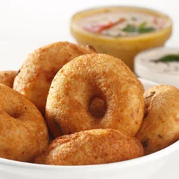 A bowl of golden-brown medu vada, with two small bowls of chutney and sambar in the background.